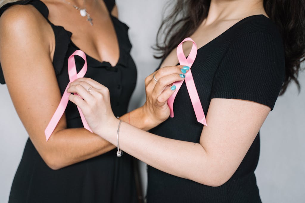 Close-up of two women holding pink ribbons symbolizing breast cancer awareness and support.