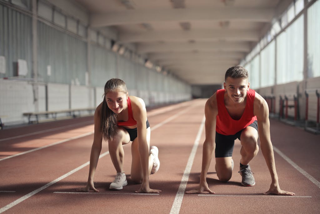 Two athletes, a man and a woman, ready to sprint on an indoor track, embodying fitness and determination.